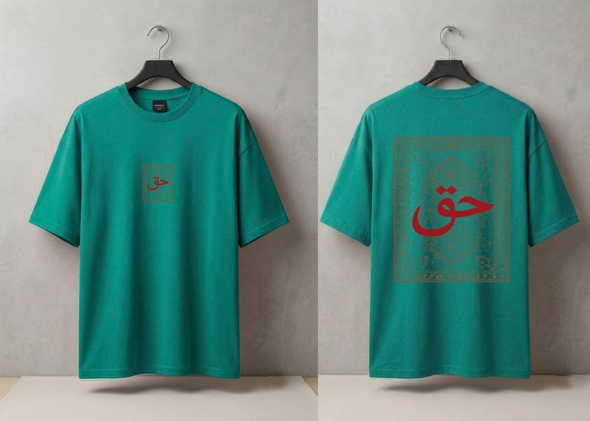 A teal green short-sleeve T-shirt shown from both front and back on black hangers against a textured light gray wall. The front has a small square chest graphic with red Arabic calligraphy.
