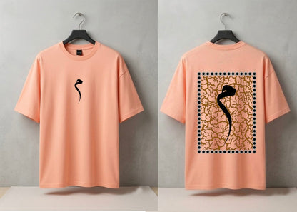 A peach-colored short-sleeve t-shirt shown from both front and back views, hanging on black hangers against a neutral gray wall. The front features a small black abstract graphic on the left chest, while the back displays a large square graphic with a black snake-like silhouette over a gold textured pattern framed by black dots.
