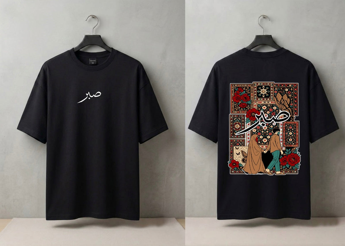A black short-sleeve T-shirt shown from both front and back on hangers against a light gray wall. The front has a small white script graphic on the left chest, and the back features a large rectangular multicolor graphic with floral and script artwork.