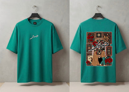 A teal green short-sleeve T-shirt shown from both front and back on black hangers against a light gray wall. The front has a small white Arabic script graphic on the left chest.