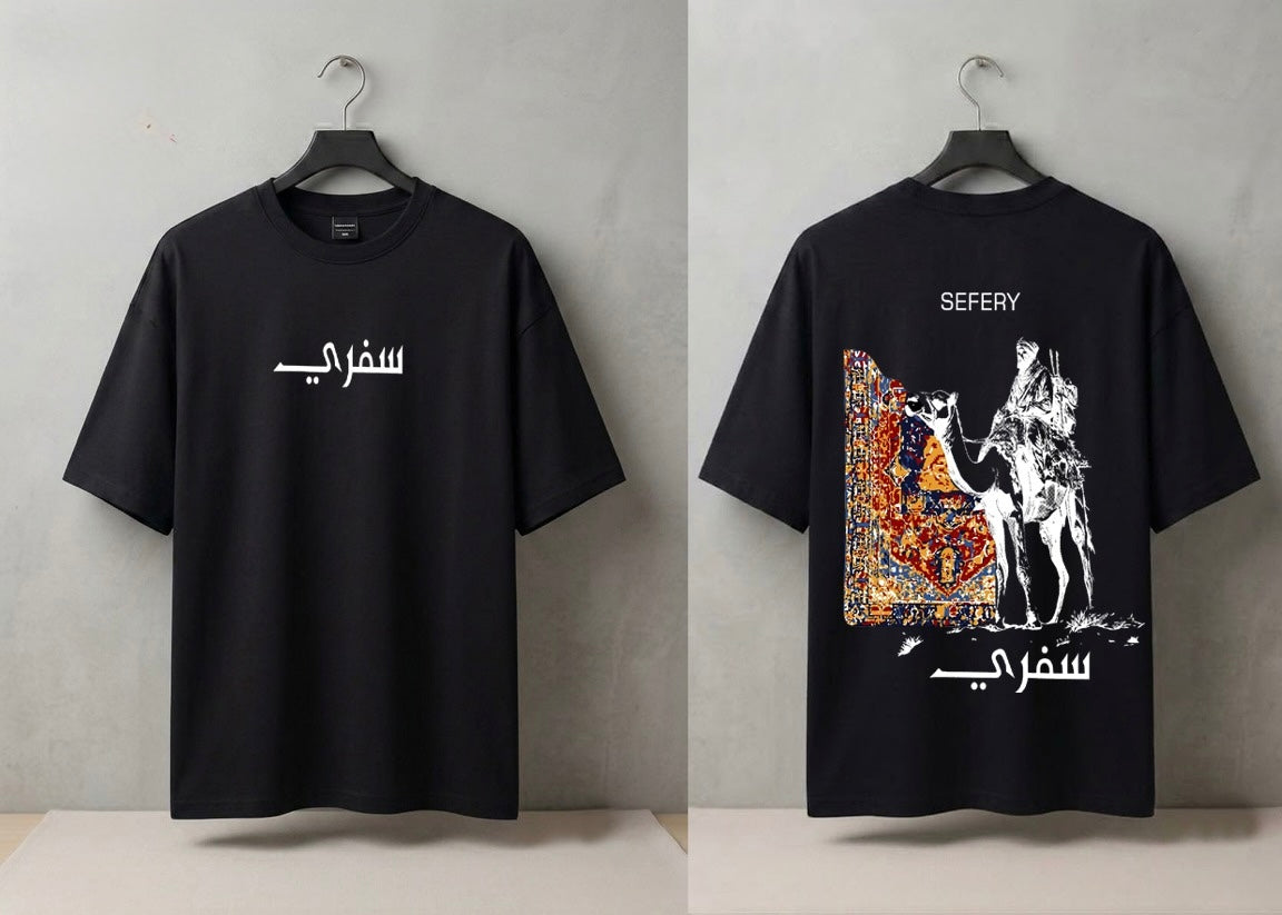 A black short-sleeve T-shirt shown from both front and back, hanging on black hangers against a light gray wall. The front has white Arabic text across the chest, and the back has a large multicolor graphic print with white line art, the word 'SEFYRY' at the top, and white Arabic text near the bottom.