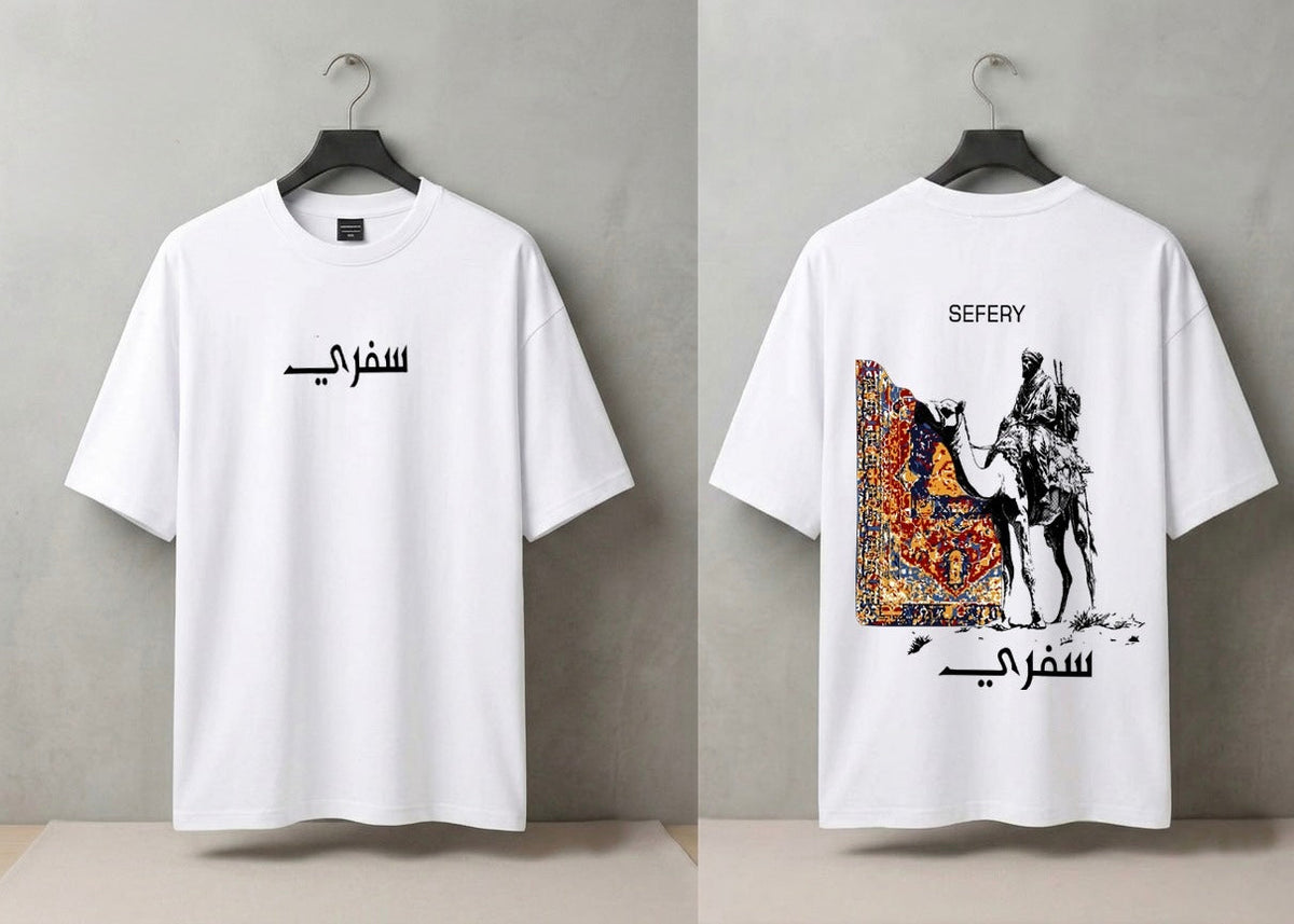 A white short-sleeve T-shirt shown from both front and back on black hangers against a gray wall. The front has black Arabic text across the chest, and the back has a large graphic print featuring a camel, rider, and ornate patterned artwork, with 'SEFERY' above and Arabic text below.