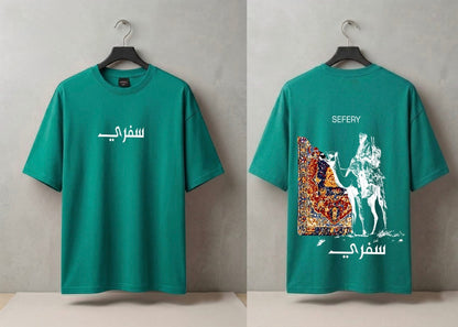 A teal green short-sleeve T-shirt shown from both front and back on black hangers against a textured gray wall. The front has white Arabic text across the chest, and the back features white Arabic text plus a large multicolor graphic print with a camel and rider motif.
