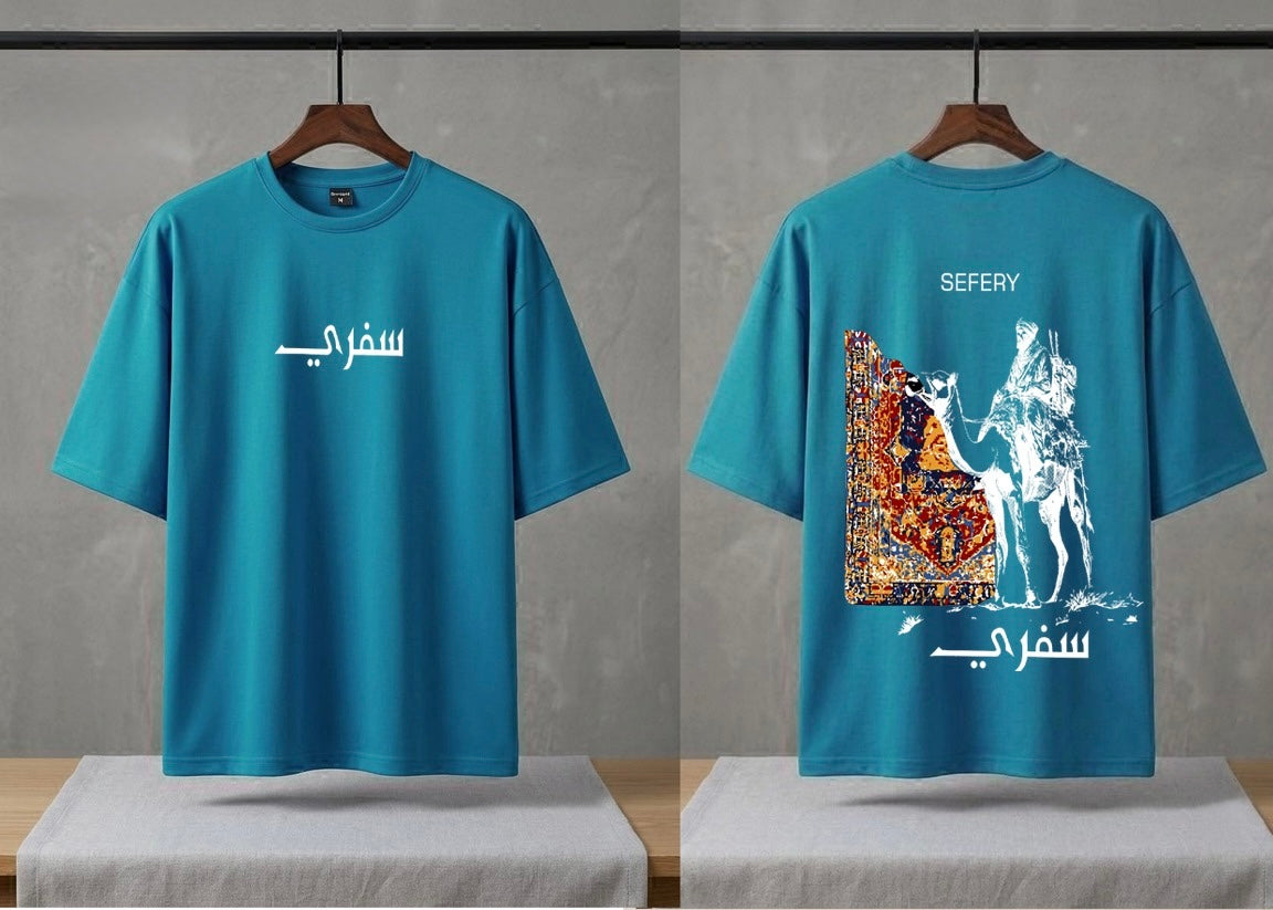 A teal blue short-sleeve t-shirt shown from both front and back on wooden hangers. The front features white Arabic calligraphy, while the back displays a large graphic print of a white horse and rider with a colorful patterned rug, alongside white English text reading 'SEFERY' and Arabic calligraphy.