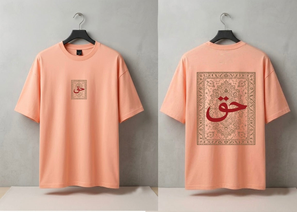 A peach-colored short-sleeve t-shirt shown from both front and back views, hanging on black hangers against a textured gray wall. The front features a small square graphic on the left chest with red Arabic calligraphy inside a beige border.