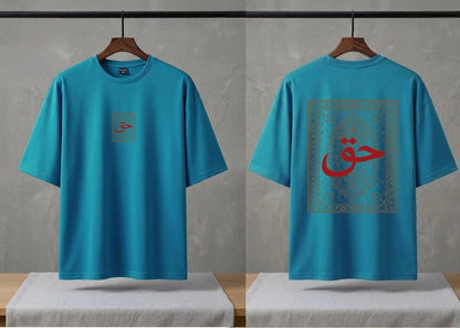 A bright turquoise blue short-sleeve t-shirt shown from both front and back views, hanging on wooden hangers against a textured gray wall. The front features a small square graphic on the left chest with red Arabic calligraphy.