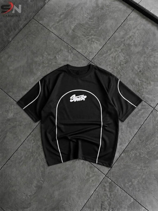 A black short-sleeve t-shirt with white contrast piping and a white graphic logo on the chest, laid flat on a dark gray tiled floor.