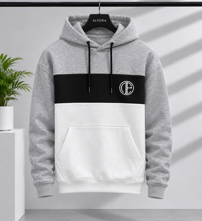 A color-block pullover hoodie hanging on a black hanger labeled ALVORA. The hoodie has a heather gray upper section and sleeves, a wide black chest band, and a white lower body and front pocket.