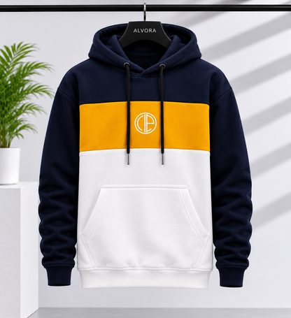 A color-blocked pullover hoodie hanging on a black hanger labeled 'ALVORA'. The hoodie features a navy blue upper section and sleeves, a mustard yellow horizontal band across the chest, and a white lower section.